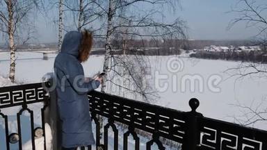 穿着蓝<strong>羽绒服</strong>的女人在冬天公园的手机里写短信。